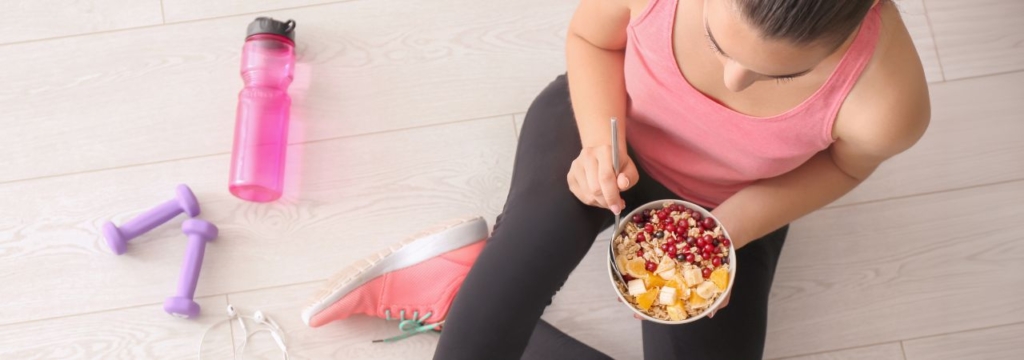 Woman eating a bowl of whole grain oatmeal and fruit before workout